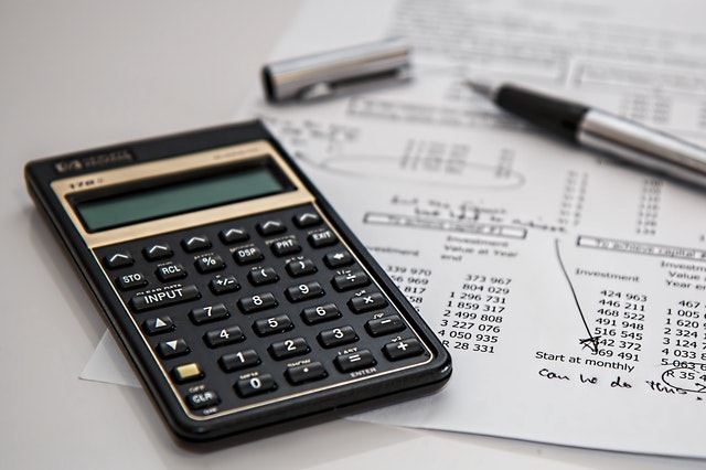 A close up of a calculator and a pen laying across a sheet of paper with numbers on it.